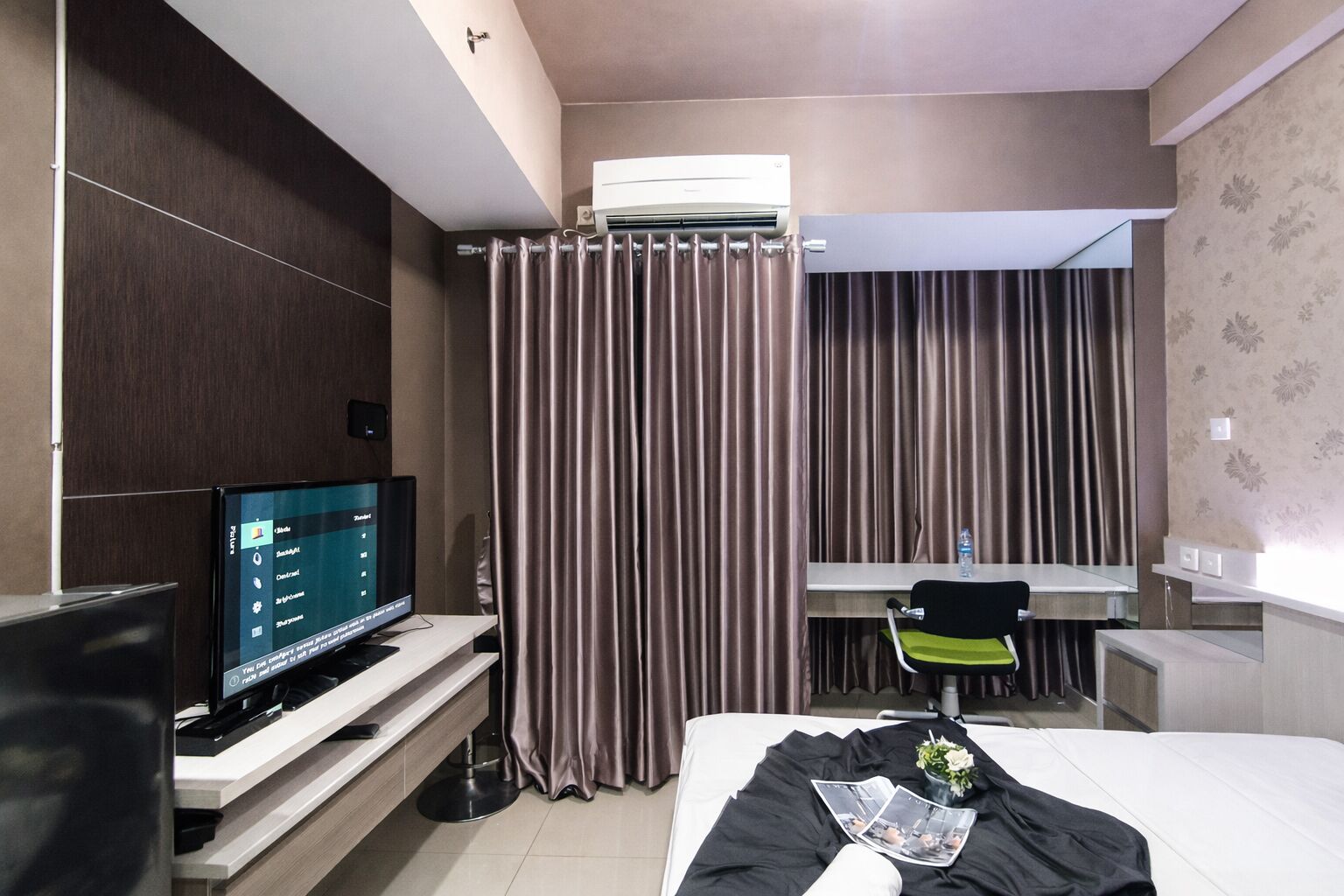 Una habitación de hotel con una cama, un escritorio con computadora, un televisor y una cortina.