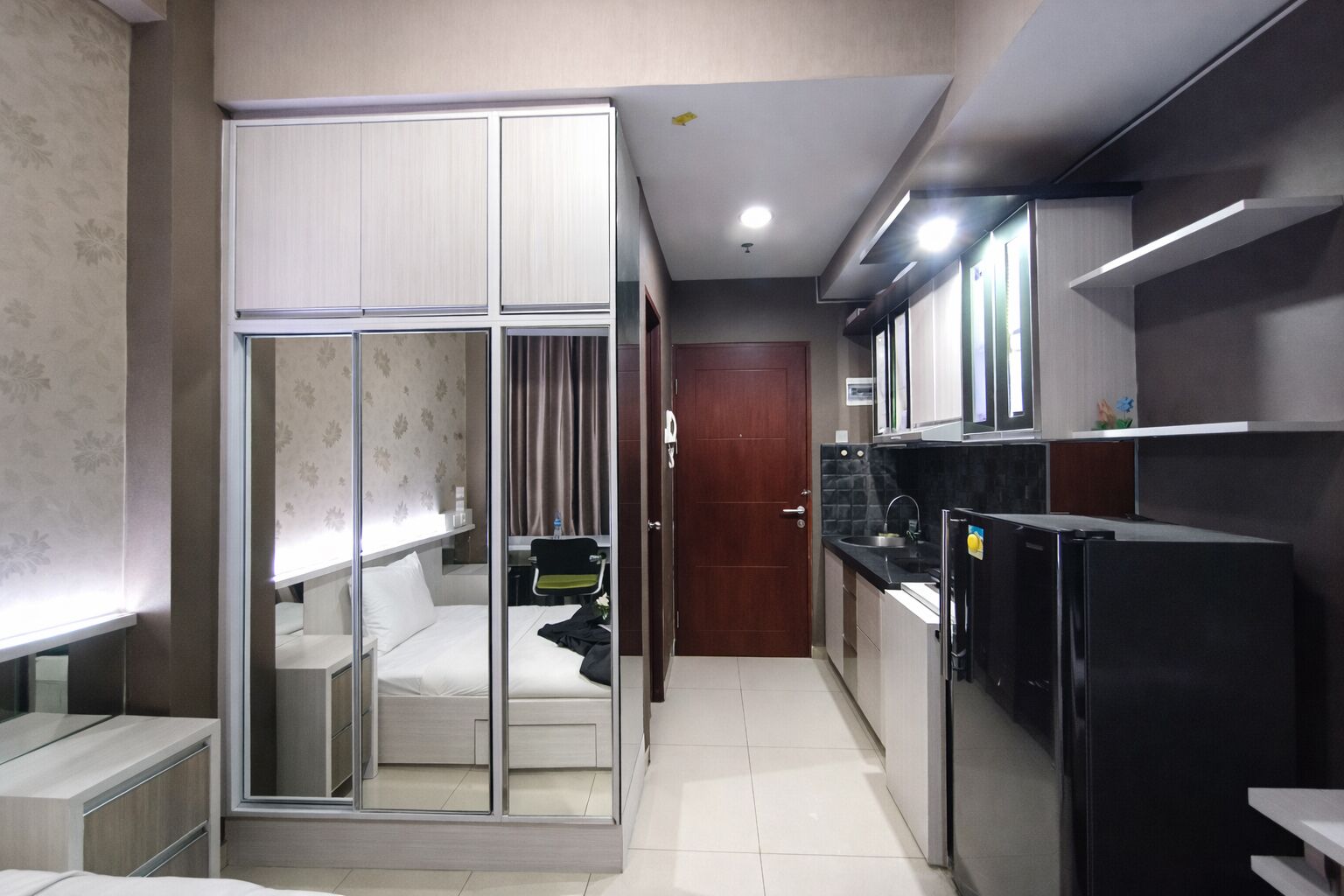 Habitació d'hotel compacta amb armari de portes corredisses, petita cuineta amb nevera i bany modest.