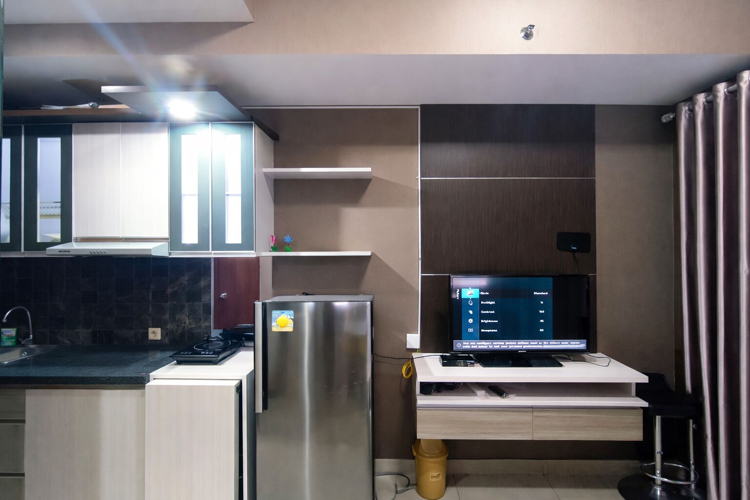 Eine moderne Küche mit Einbauherd, Kühlschrank und Wand-Fernseher, der eine Speisekarte zeigt.