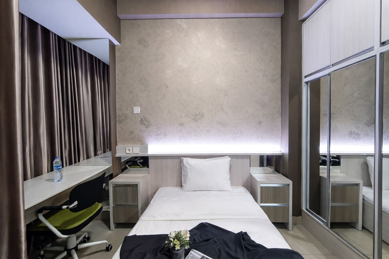 A hotel room with a bed, two bedside tables, a desk with a chair, a mirror, and a water bottle on the desk.