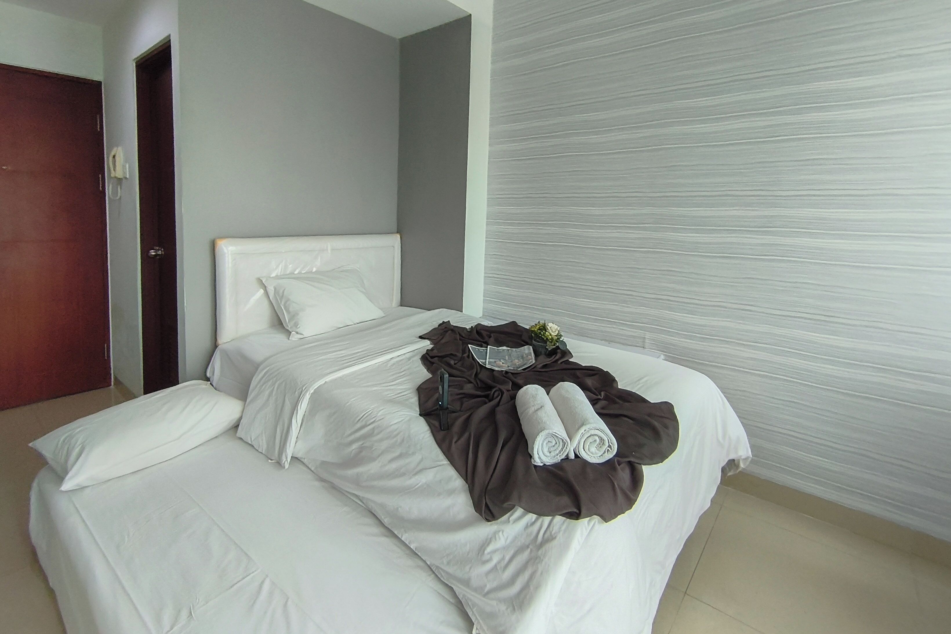 A neatly made bed with white linens, a brown blanket, and rolled towels.