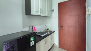 A kitchen with a refrigerator, a sink, cabinets, and a door. - Comfortable Gray Studio Room At Apartment Taman Melati Jatinangor (Hegarmanah)