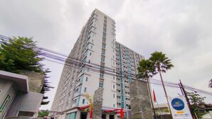 A tall, multi-story building with a modern architectural design, featuring a prominent entrance with a red canopy. - Comfortable Gray Studio Room At Apartment Taman Melati Jatinangor (Hegarmanah)