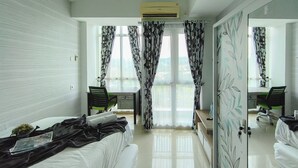A hotel room with a bed, a desk, a chair, and a large mirror. - Comfortable Gray Studio Room At Apartment Taman Melati Jatinangor (Hegarmanah)