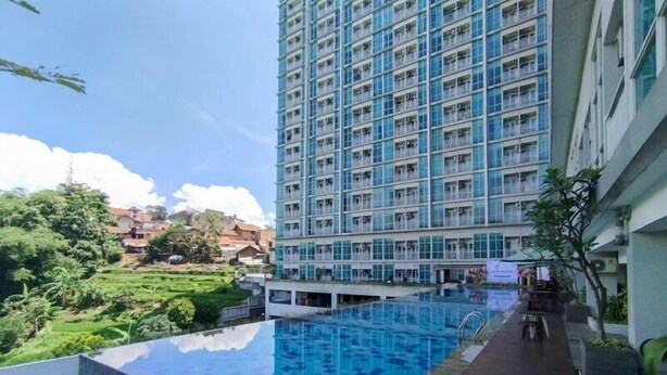 A high-rise hotel with a rooftop infinity pool, a view of the surrounding landscape, and a large building in the background. - Comfortable Gray Studio Room At Apartment Taman Melati Jatinangor (Hegarmanah)