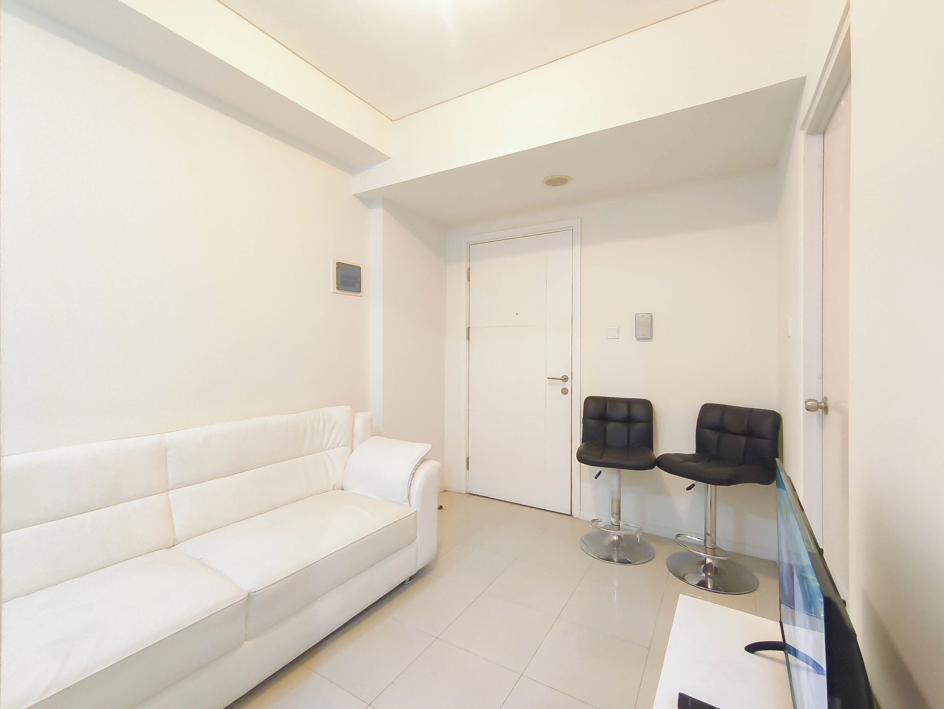 A white sofa, two black chairs, a closed door, and a small picture frame on the wall.