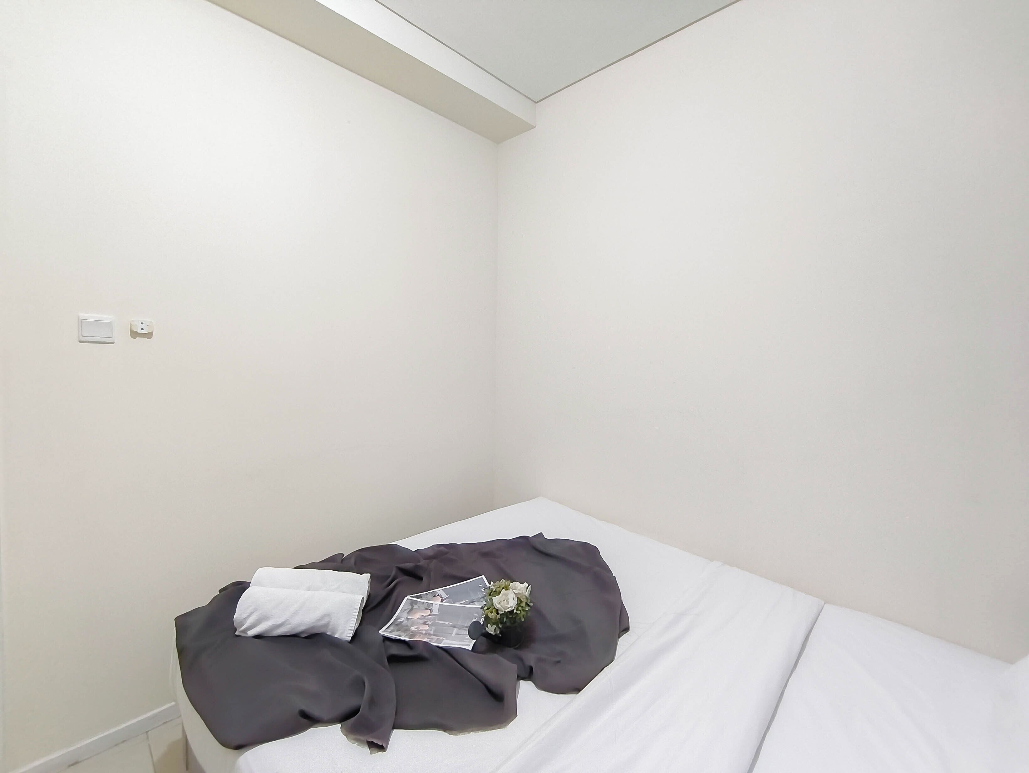 A small, clean room with a single bed, a white wall, and a power outlet.