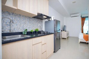 A modern kitchen with a black countertop, stainless steel appliances, and wooden cabinets. - Calming And Restful Studio At Apartment Grand Kamala Lagoon (Bekasi)