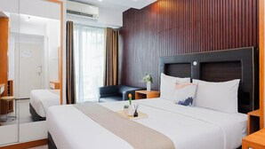 A hotel room with a large bed, a bedside table, a chair, a mirror, and a wooden panel wall. - Good And Comfy Studio Apartment At Grand Kamala Lagoon (Bekasi)