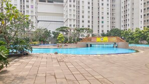 A swimming pool surrounded by a tiled deck, with a building in the background. - Comfortable And Homey 2Br At Apartment Green Bay Pluit (Jakarta)