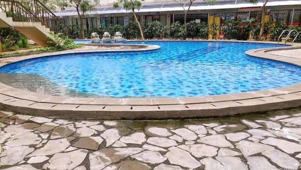 A swimming pool with a stone border, surrounded by a building with a staircase and greenery. - Practical 2Br For 3 Pax At Kebagusan City Apartment (Jakarta)