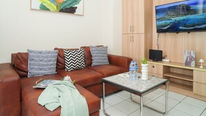 A living room with a brown leather sofa, patterned cushions, a small table with a vase, a water bottle, and a framed picture. - Practical 2Br For 3 Pax At Kebagusan City Apartment (Jakarta)