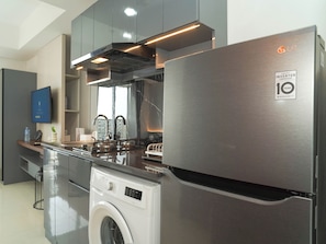 A modern kitchen with stainless steel appliances, a washing machine, and a flat-screen TV. - Neat Urban Style Studio Room At Apartment West Vista (Jakarta)