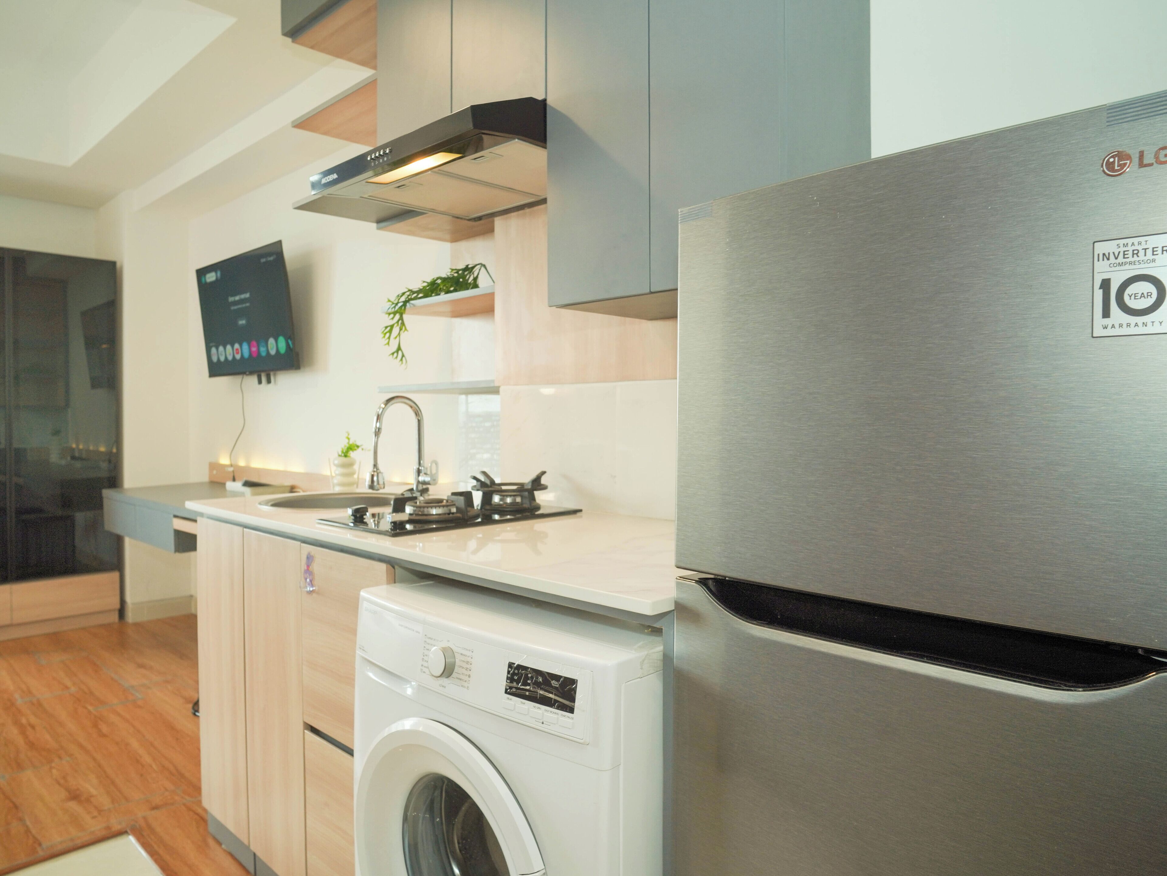Una cocina moderna con electrodomésticos de acero inoxidable, lavadora integrada y un televisor de pantalla plana.