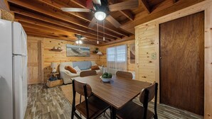 A wooden cabin interior with a dining table, chairs, a ceiling fan, and a refrigerator. - Cozy 1-bedroom cabin in perfect Hudson with cool AC (Hudson)