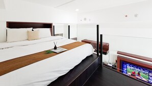 Quarto de hotel com cama, mesa de cabeceira de madeira, televisão e janela.