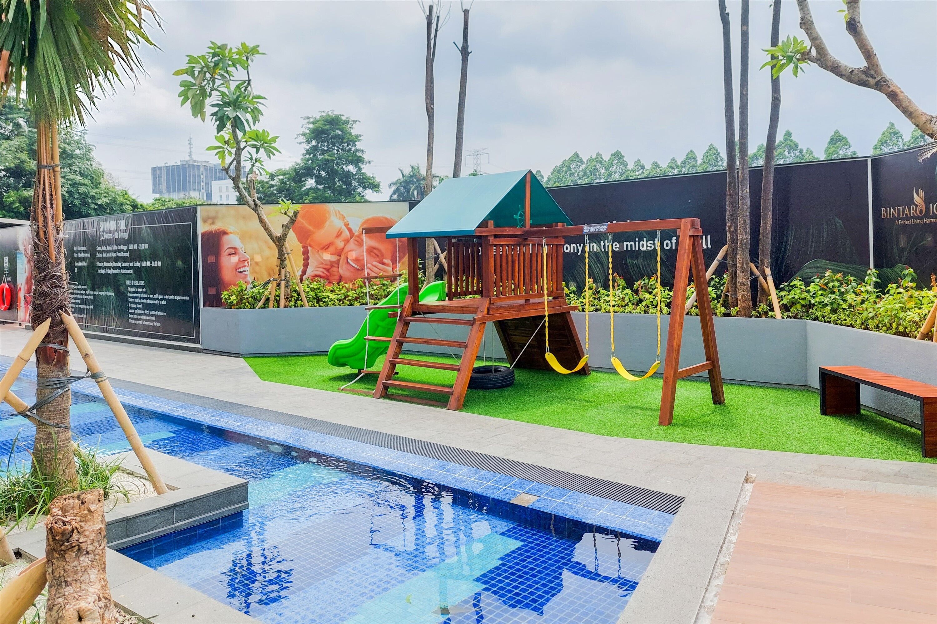 Una piscina con un parque infantil de madera y un tobogán verde.