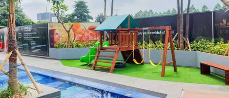 Una piscina con un parque infantil de madera y un tobogán verde.