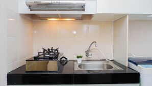 A modern kitchen with a gas stove, a stainless steel sink, and a built-in range hood. - Enjoy Restful Living In Studio Room At Apartment Oasis Cikarang (Cikarang)