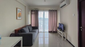 A living room with a sofa, a TV, a white table, and a water bottle. - Neat And Restful 2Br At Gateway Pasteur Apartment (Cimahi)