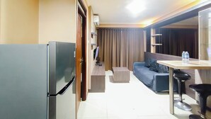 A hotel room with a refrigerator, a television, a sofa, a small table, and a mirror. - 4 Pax Warm Brown 2Br At Gateway Pasteur Apartment (Cimahi)