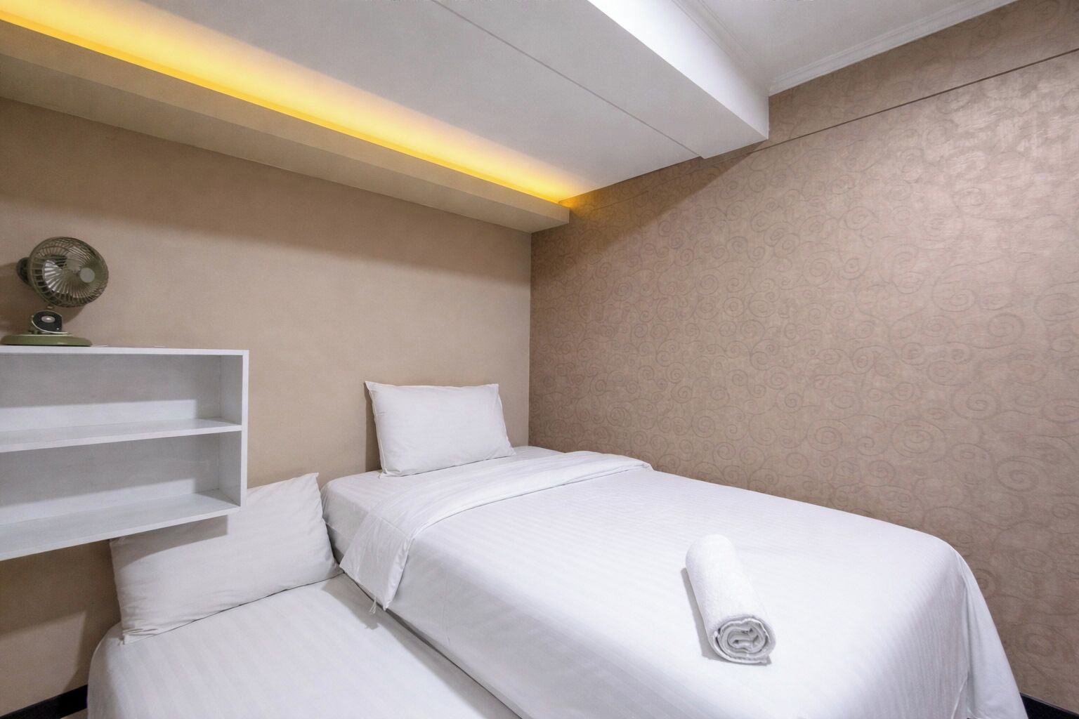 A hotel room with a bed, a shelf, and a wall fan.