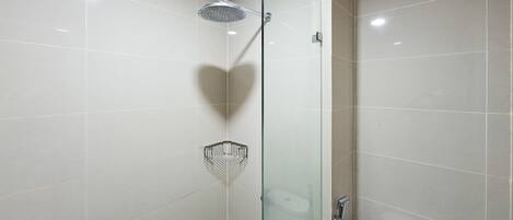 Et moderne badeværelse med en glasafskærmet brusekabine, toilet og en lille hylde.