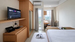 Habitació d'hotel amb un llit, una taula de treball amb un ordinador, un televisor sobre una estantalia i vista cap a l'exterior.