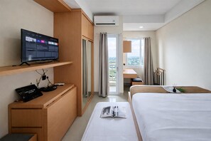 Ein Hotelzimmer mit Bett, Schreibtisch mit Computer, Fernseher auf einem Regal und Blick ins Freie.