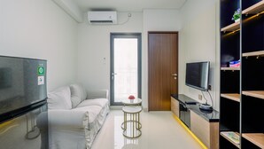 A modern hotel room with a sofa, a TV, a small table with a flower, and a wardrobe. - Comfortable 1Br With Extra Room At Transpark Cibubur Apartment (Bekasi)