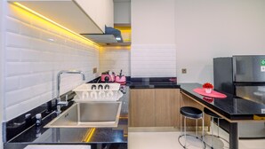 A modern kitchen with a black countertop, stainless steel appliances, and a white tiled backsplash. - Comfortable 1Br With Extra Room At Transpark Cibubur Apartment (Bekasi)