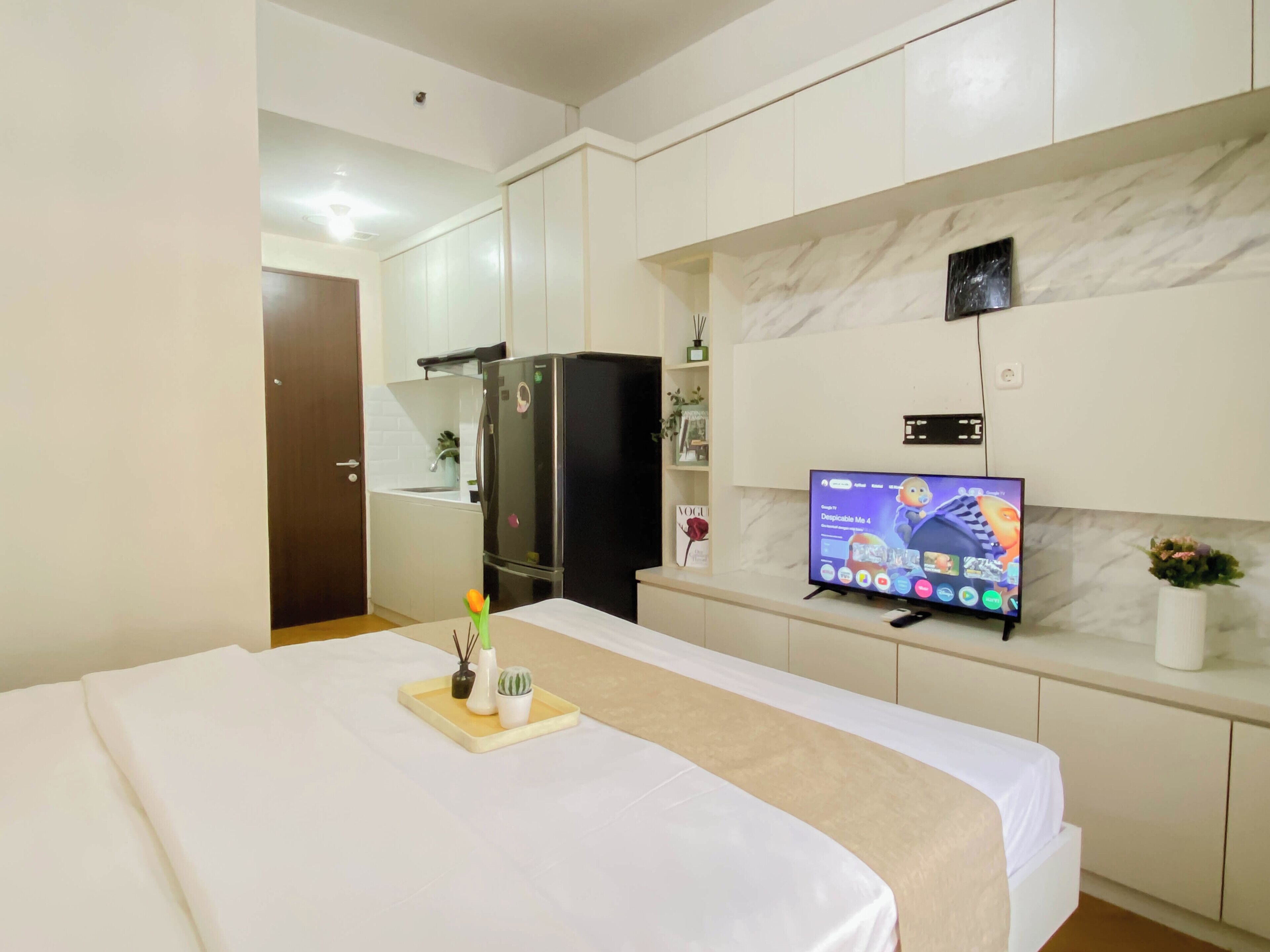 Una habitación de hotel con cama, televisión, minibar y puerta.