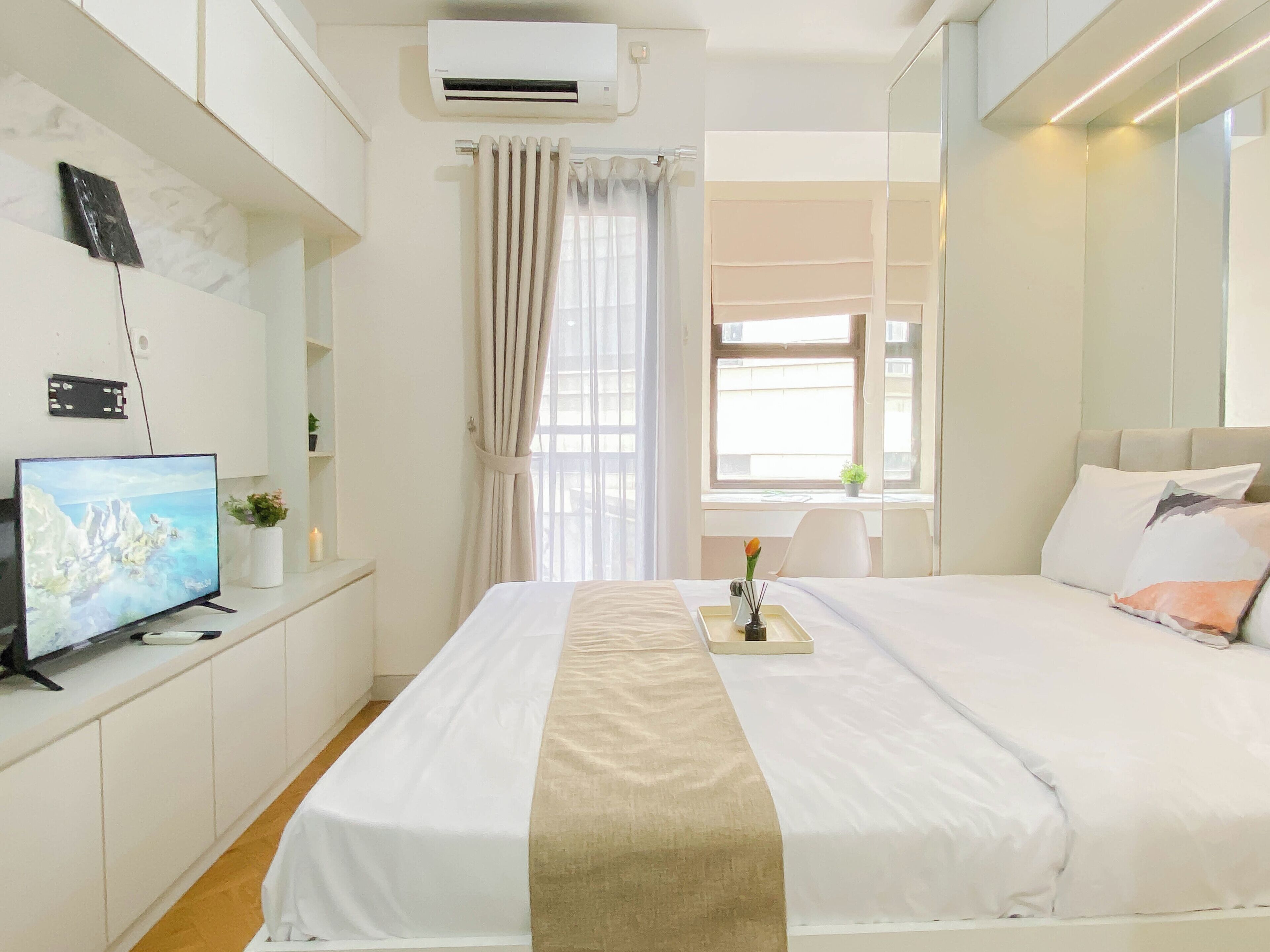 Una habitación de hotel con una cama, televisión, ventana con cortinas, mesita de noche con una planta y un equipo de aire acondicionado.