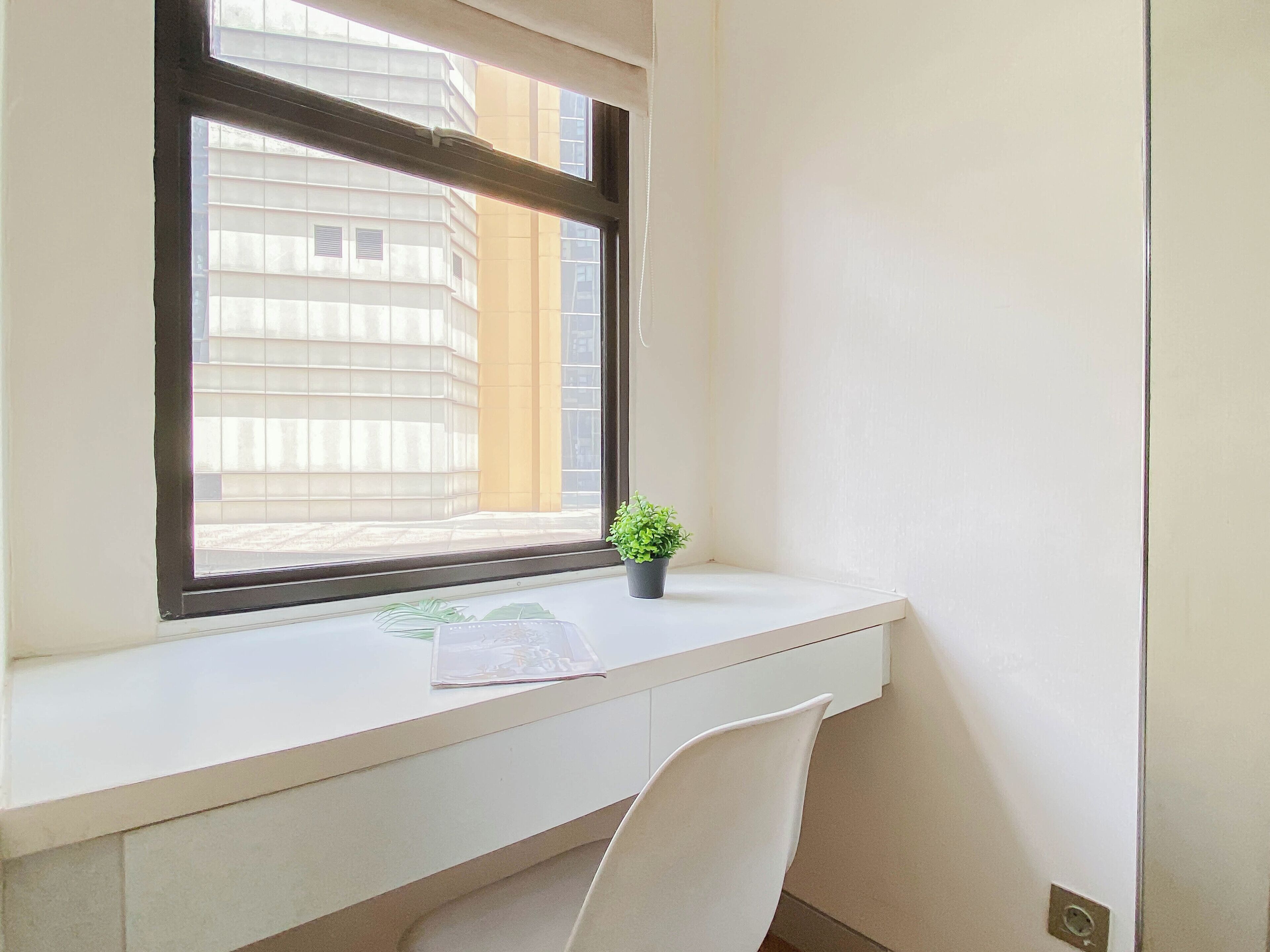 A room with a window, a desk, a chair, and a small potted plant.