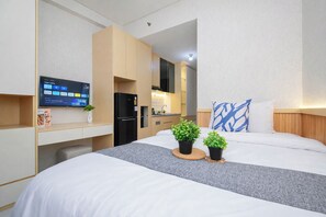 A hotel room with a bed, a desk, a TV, a refrigerator, and a small kitchen area. - 2 Pax Practical Studio At Transpark Cibubur Apartment (Bekasi)