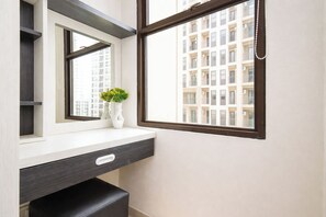 A bathroom with a white vanity, a mirror, a window with a view of a building, and a vase with flowers. - Bright And Comfy Studio Apartment At Transpark Cibubur (Depok)