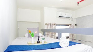Habitación de hotel con cama, toalla azul, almohada blanca, un jarrón con flores y una pequeña planta.
