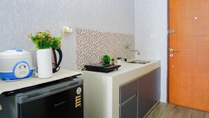 Una cocina compacta con microondas, hervidor y pequeñas plantas sobre la encimera.
