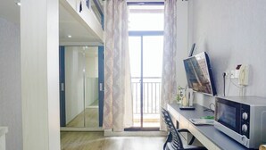 Una habitación moderna con escritorio, microondas, silla, ventana con cortinas y vistas al exterior.