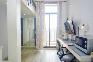 Ein modernes Zimmer mit Schreibtisch, Mikrowelle, Stuhl und einem Fenster mit Vorhängen sowie Blick nach draußen.