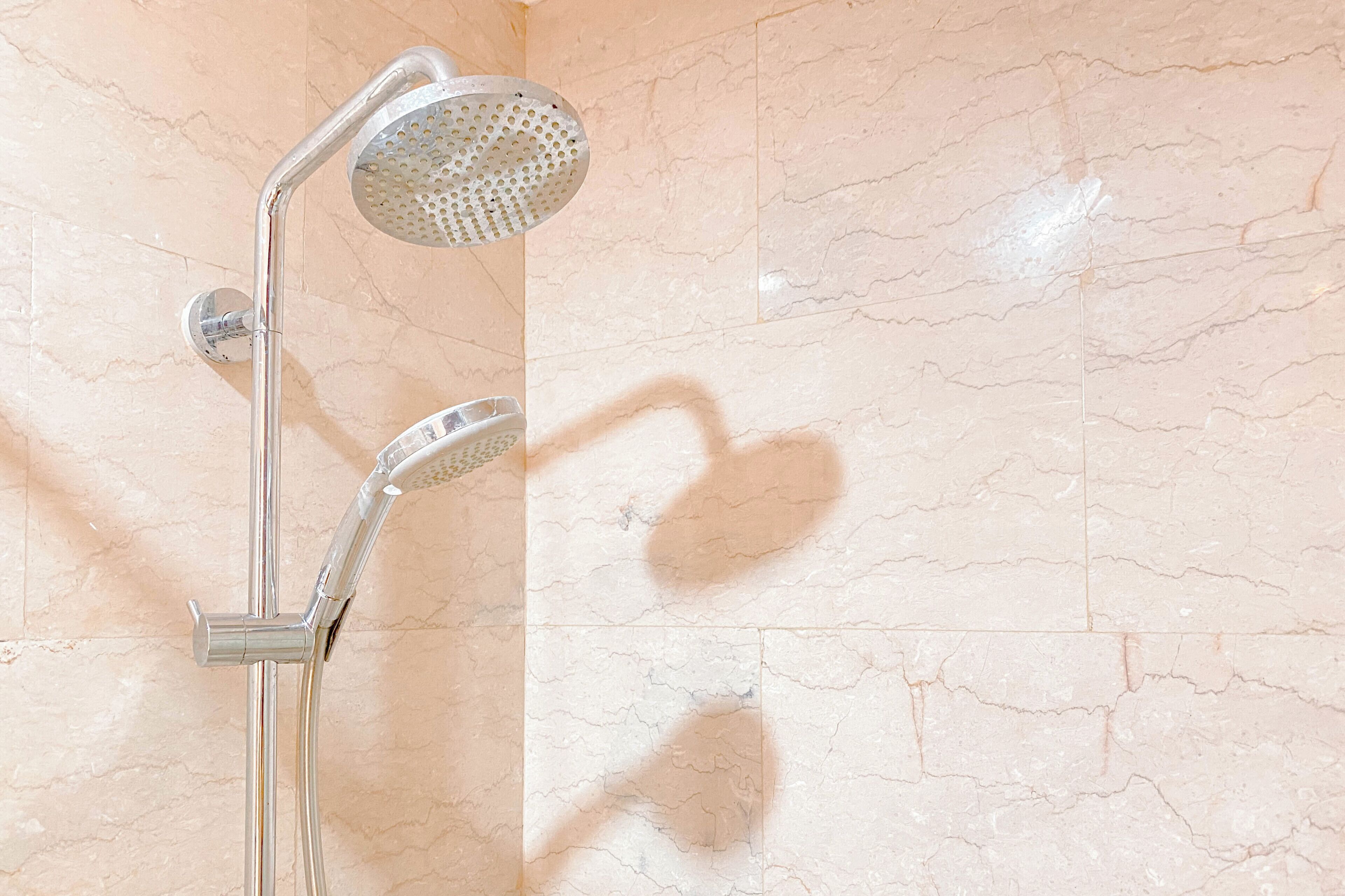 Une douche équipée d’un pommeau de douche à main et d’un pommeau de douche fixe, le tout fixé sur un mur recouvert de carreaux imitant le marbre.