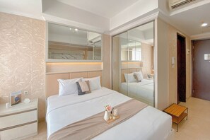 A hotel room with a large bed, a nightstand, a bedside table, a mirror, and a wardrobe. - Peaceful Beige Studio At Menteng Park Apartment (Jakarta)