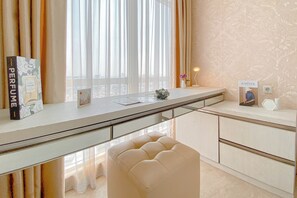 A modern room with a glass desk, a cushioned bench, a perfume box, a framed picture, and a small vase with flowers. - Peaceful Beige Studio At Menteng Park Apartment (Jakarta)