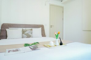 Ein ordentlich bezogenes Bett mit Holz-Kopfteil, zwei Kissen, einem Tablett mit einer weißen Kerze, einer kleinen Vase mit Blumen und einer Zeitschrift auf dem Bett.