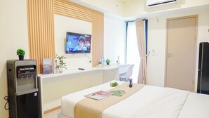 Habitación de hotel con cama, escritorio con computadora, dispensador de agua, televisor y puerta.