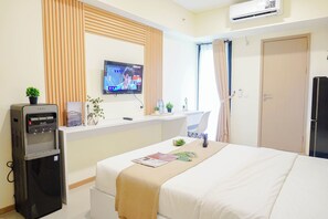 Ein Hotelzimmer mit Bett, Schreibtisch mit Computer, Wasserspender, Fernseher und Tür.