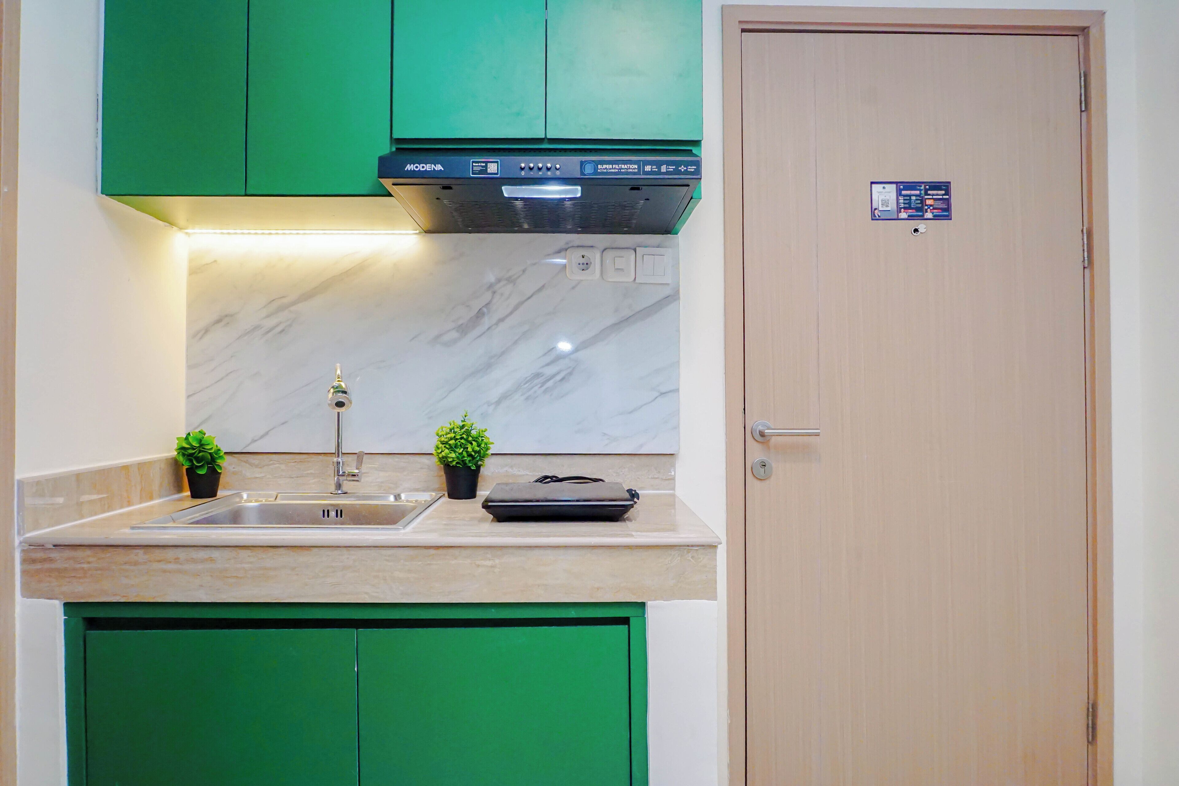 A kitchen with green cabinets, a marble backsplash, a built-in oven, and a door with a lock.