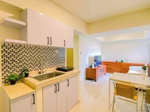 A modern kitchen with white cabinets, a tiled backsplash, and a dining area with a table and chairs. - 2Br Near Aeon Deltamas At Meikarta Apartment (Cikarang)