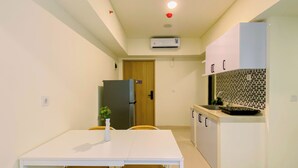 Uma cozinha compacta com uma mesa branca, duas cadeiras, uma geladeira, painel atrás do fogão em azulejo e uma porta que dá para outro cômodo.