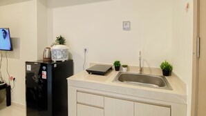 A compact kitchen with a refrigerator, a coffee maker, a sink, and a small potted plant. - Comfortable And Minimalist Studio At Apartment Meikarta District 1 (Cikarang)